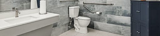 A bathroom with a white sink, toilet, and a grey tiled wall.