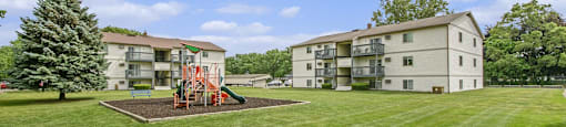 a playground in the middle of a grass field next to an apartment building