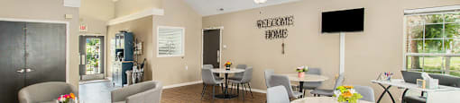 a living room with tables and chairs and a kitchen with a tv