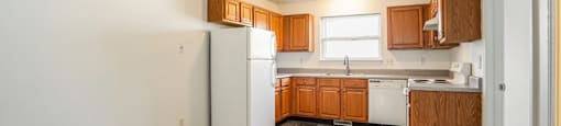 A kitchen with a white refrigerator, wooden cabinets, and a tiled floor.