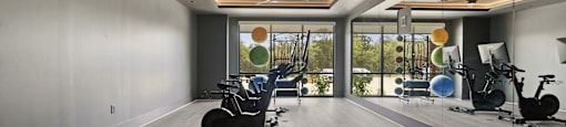 A spacious room with a ceiling fan, exercise equipment, and a view of trees outside the window.