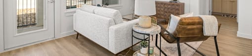 A living room with a white sofa and a chair with a brown cushion.