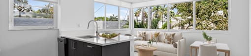 A modern kitchen with a large island and a view of the outdoors through the windows.