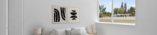 A bedroom with a large bed and two abstract paintings on the wall.