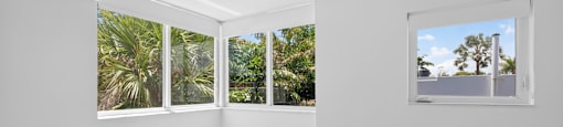 A white room with a marble floor and windows overlooking a tropical landscape.