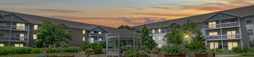 A sunset view of apartment buildings with a grassy area in the foreground.
