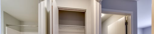 Apartment with white closet with shelves and a door open to a hallway.