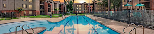 A swimming pool in front of apartment buildings at sunset.