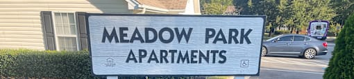 A sign for Meadow Park Apartments is displayed in front of a house.