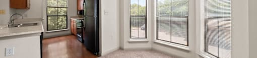 a living room with a large window and a kitchen in the background