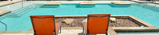 a pool with two orange lounge chairs and a swimming pool with trees in the background