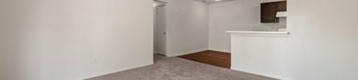 an empty living room with a kitchen in the background