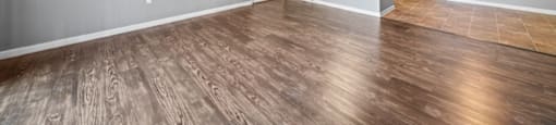 an empty living room with a ceiling fan and a kitchen in the background