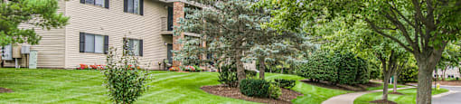 a walkway through a grassy area with trees and a building in the background