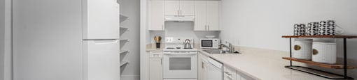 A white kitchen with a refrigerator on the left and a sink with a faucet on the right.