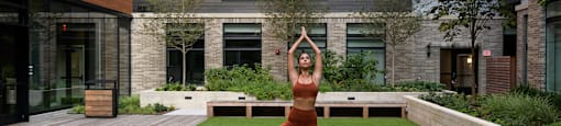 A woman in a yoga pose on a green lawn in front of a building at Arrowwood Apartments, North Bethesda