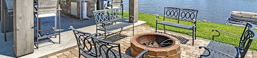 a patio with a fire pit and chairs next to a lake  at Lakeshore Pointe Apartment Homes, Brandon