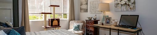 A bedroom with a bed, desk, and a window with blinds.