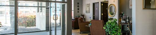 A glass door with a handle is open to a room with a chair and a potted plant.