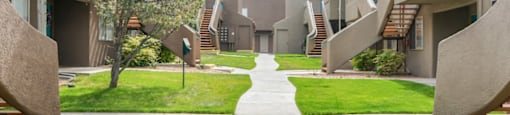 A concrete pathway leads through a grassy area between two rows of concrete buildings.