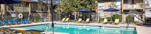 A pool with yellow chairs and blue umbrellas.
