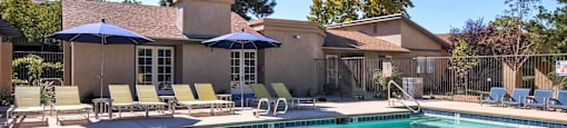 A pool with a blue umbrella and chairs.