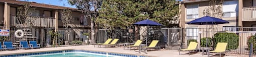 A swimming pool with a blue umbrella and yellow chairs.