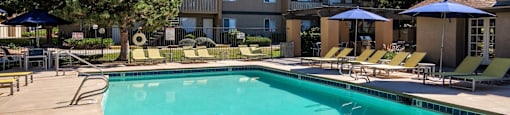 A large swimming pool with sun loungers and umbrellas in front of a building.