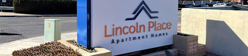 A blue and white sign for Lincoln Place Apartment Homes sits in front of a building.
