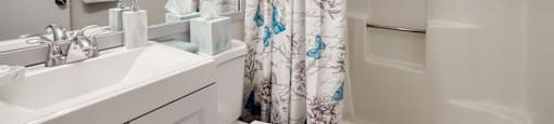 A white bathroom with a sink, mirror, and shower curtain.