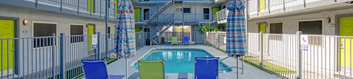 A pool surrounded by chairs and umbrellas in a courtyard.