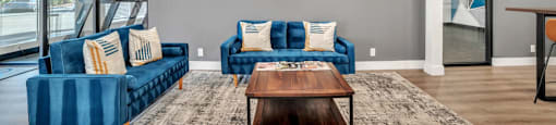 A living room with blue couches and a large painting on the wall.