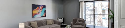 A living room with a grey couch, a brown armchair, and a painting on the wall.