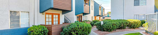 A row of modern townhouses with a sidewalk and green grass in front.