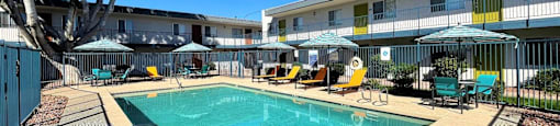 A swimming pool surrounded by chairs and umbrellas in a sunny day.