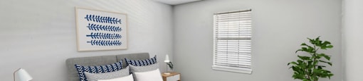 A bedroom with a bed, nightstand, and a plant.