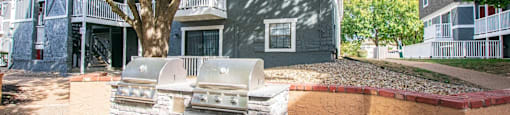A sandbox with a small building and a tree in front of a grey building.