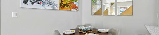 A dining room with a table set for two and a large abstract painting on the wall.