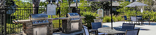 a patio with a barbecue grill and tables with umbrellas