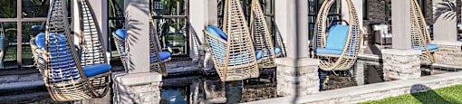 a row of hanging wicker hammocks in front of a building with a pool