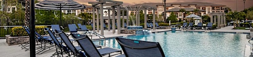 a swimming pool with chairs and umbrellas at sunset