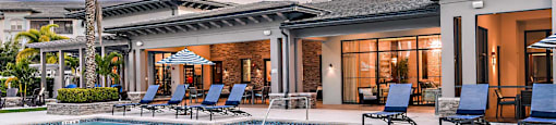 a large swimming pool with chairs and a building in the background