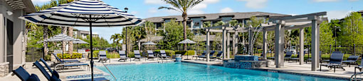 A pool with a striped umbrella and lounge chairs.