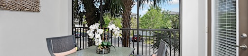 A patio with a glass table and chairs overlooking a tree.