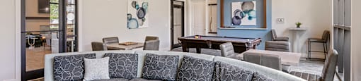 A grey patterned sofa sits in a spacious living room with a large painting on the wall.