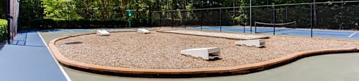 a tennis court with two benches on it and trees in the background