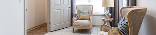 a living room with two chairs and a table with a lamp