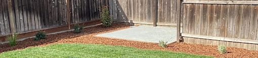 A backyard with a wooden fence and a green lawn.