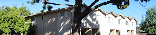 The side view of the aegena apartments a beige building with garage entrances and cars parked in a slanted direction in front of the building Prodesse Property Group 1211 Garbo Way  San Jose, CA 95117