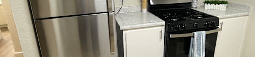 A stainless steel refrigerator is in a kitchen with white cabinets and a black stove.